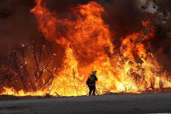 A firefighter standing in front of massive flames from the Line Fire