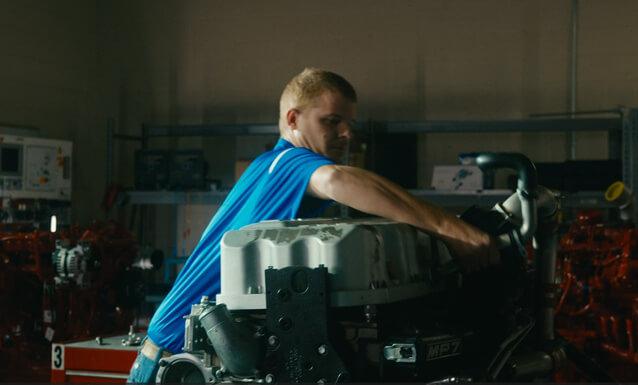 A side profile of an auto mechanic student working on an engine